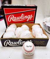 Ten new Rawlings genuine leather Little League baseballs wrapped in paper in the original branded cardboard Rawlings box, with one ball displayed outside the box showing branding.