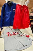 Full view of all three Phillies apparel items: blue jacket, red pullover shirt, and gray jersey