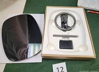 Image showing all components of Presence Inspiration Display including black reflective display screen, metal ring base, metal assembly pole, and power adapter in foam packaging.