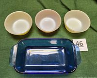 Photo showing three small milk glass Federal Glass Company bowls in light yellow, dark yellow, and salmon color, positioned above the cobalt blue Pyrex loaf pan on green fabric background.