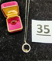 Photo showing the gold-filled pinky ring in an open red and gold lined jewelry box next to the sterling silver necklace with circle pendant containing five gold stars on a black background.