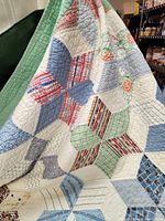 Detailed view of quilt showing star pattern with blue, red, green, and cream fabric patches and visible hand quilting.