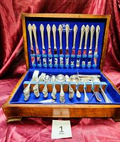 Opened wooden tarnish-resistant chest with blue felt lining showing 98 pieces of 1847 Rogers Bros Remembrance pattern silverplate silverware arranged neatly.