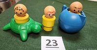 Three Little People jumbo figures with round painted heads and yellow bases beside green turtle and blue pitcher boat bathtub toys shown on green cloth surface.