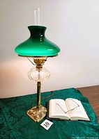 Full view of the antique table lamp on a green patterned cloth surface with an open book and glasses beside it for scale.