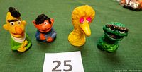 Front view of four vintage Sesame Street finger puppets on green background showing Oscar the Grouch, Big Bird, Bert, and Ernie.