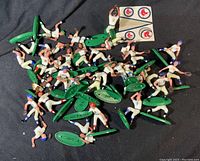 Spread of 28 toy baseball figures with green bases and a sheet of team logo stickers