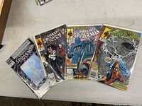 Four Amazing Spider-Man Marvel comic books laid out on a table, each in a clear protective sleeve. Issues 328, 329, 330, and 365 are visible with colorful covers.