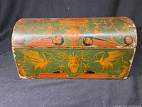 Front view of the painted wooden box showing bird and crowned face motifs