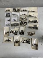 Overview of the full lot showing 26 vintage car photographs spread on a flat surface, various sizes, black and white, some curling visible.