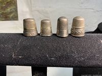 Four antique sterling silver thimbles arranged in a row showing varied embossed patterns and size differences.
