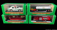 Front and top view of four new in box Hess miniature toys including patrol car, tanker truck, voyager boat, and fire truck in original unopened packaging.