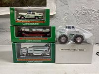 Front view of the four Hess miniature toy collectibles with three boxed and the Bobcat in plastic wrap placed atop a white box.