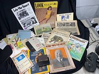 Photo of various ephemera items laid out on black cloth background including magazines, programs, letters, maps, and booklets.
