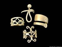 Four vintage sterling silver rings grouped on black background, showing varied designs including wide wrap-around and openwork styles.