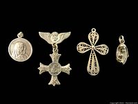 Four sterling silver religious charms including Virgin Mary, angel cross pin, filigree cross, and Virgin Mary face charm on black background.