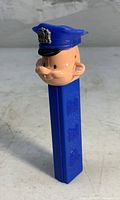 Front angle view of vintage Pez policeman dispenser showing blue stem and policeman head with badge on hat.
