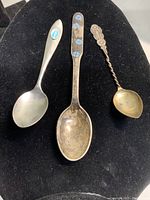Three sterling silver collector spoons displayed on black background showing size and design variety.