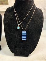 Two sterling silver necklaces displayed on a black bust, one with a turquoise pendant and the other with a striped glass pendant.