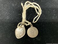 Two vintage sterling silver pendants tied with string on black background, showing front sides with floral and ornamental engravings.