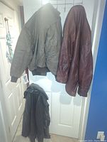 Two leather jackets hanging on door. One is brown with quilted pattern; other is darker brown with smooth finish.