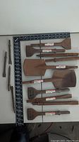 Photo showing multiple hammer drill attachments laid out next to a ruler for size reference, including several flat spade chisels and pointed chisels with metal shanks.
