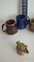 Four mugs in assorted colors and patterns with a small decorative pottery rattle in front
