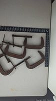 Five large metal C clamps arranged on a white surface next to a ruler to show size. The clamps are rusty and need cleaning.