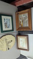 View of all four lighthouse-themed artworks including watercolor, wood-burned plaque, and two framed pieces with dried plants and sketches.