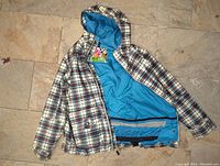 Plaid hooded snow jacket with blue interior lining laid flat on tiled floor, showing interior and exterior.