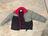 Red, green, and black color-block men's insulated winter jacket laid flat showing full front and sleeves spread out.