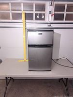 Front view of the closed mini fridge showing stainless steel finish with black trim.