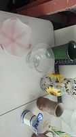 View of all items on table including sunflower pitcher, green pitcher, pottery vase, brown pitcher, and clear glass bowl