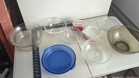 View of several glass dishes and bowls including clear Pyrex glass and one blue dish along with an opaque large bowl and a small square plastic container with red contents.