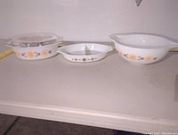 Front view of the three Pyrex bakeware pieces with floral pattern showing the casserole dish with lid, oval divided dish, and round handled bowl