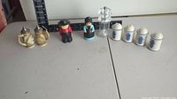 Full view of all salt and pepper shakers included in the lot showing Budweiser stein set, figurine pair, clear plastic grinder, and Blue Onion ceramic set.