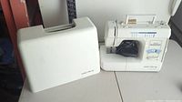 Euro-Pro X sewing machine next to its white hard plastic carrying case on a gray tabletop.