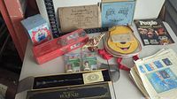 Photo showing assortment of collectible items on a table including a Major League baseball card set, magic wand box, novelty purse, vintage magazines, and decorative items.