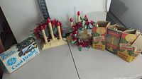 Vintage Christmas decorations including candle wreaths, electric candle holder, GE Cool Bright lights and boxes of Noma light fixtures on a table with a ruler for scale