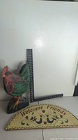 View of wooden chicken figurine next to a metal square and the wooden sign showing 'Welcome Friends'.