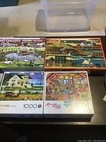 Four 1000-piece puzzle boxes on display including Art Gallery, a village scene, Charles Wysocki cottage, and Aimee Stewart Collection puzzles