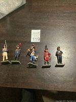 Five die-cast solder soldiers, all standing on rectangular bases, arranged on a dark wood surface