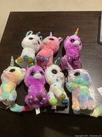 Seven colorful Ty Beanie Boos unicorn plush toys arranged on a table with tags attached, showing variety of colors and glittery details on horns and feet.