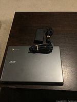 Closed Acer Chromebook laptop with charger and power cable on a dark wood table.