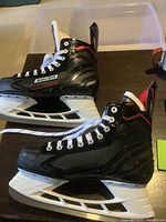 Side view of both Bauer men's ice hockey skates in black with white and red accents, showing the Tuuk blades and size 9 marking.