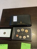 Photo showing black Royal Canadian Mint presentation box with gold logo, certificate of authenticity folder, and clear protective coin set case containing seven coins.