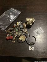 Full view of assorted costume jewelry pieces arranged on a dark surface including charms, pins, bracelets, and a ring.