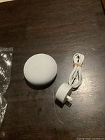 Google Nest Mini smart speaker with fabric top, white power adapter, and white cable neatly coiled with rubber band on wood surface.