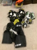 Full set of junior medium hockey equipment including pants, shoulder pads, elbow pads and gloves arranged on carpet floor