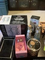 Photo showing boxed 3-piece glass serving tray set, black jewelry box, pink wine glass in box, two decorative glass bottles with cork stoppers, and small gold decorative container.